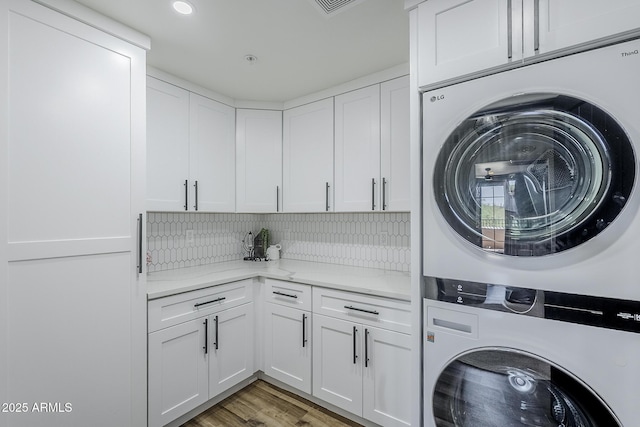laundry room featuring stacked washing maching and dryer, light wood finished floors, and cabinet space