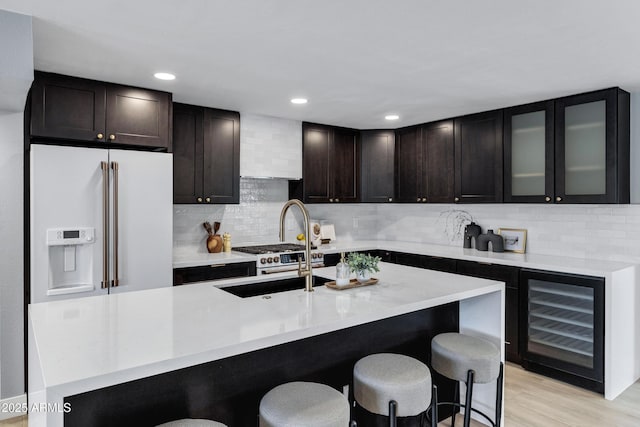 kitchen featuring sink, dark brown cabinetry, high end fridge, light wood-type flooring, and beverage cooler