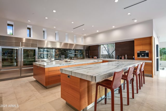 kitchen with light stone countertops, backsplash, a kitchen bar, and a spacious island