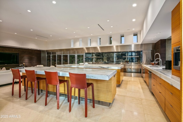 kitchen featuring sink, a breakfast bar area, tasteful backsplash, a large island, and light stone countertops