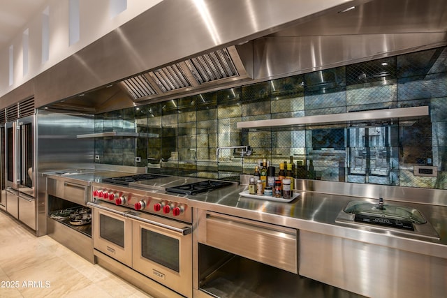 kitchen with wall chimney range hood, backsplash, light tile patterned floors, and range with two ovens