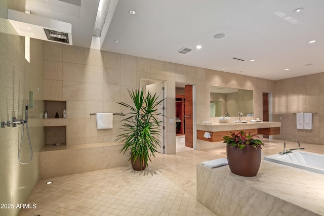 bathroom featuring a relaxing tiled tub, vanity, and tile walls