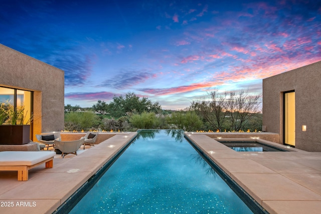 pool at dusk with an in ground hot tub and a patio area