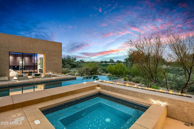 pool at dusk with an in ground hot tub