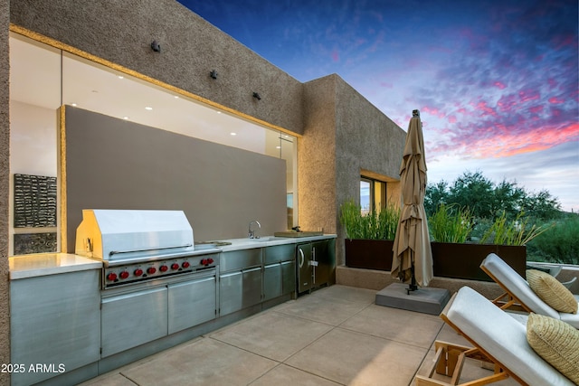 patio terrace at dusk featuring exterior kitchen, sink, and grilling area