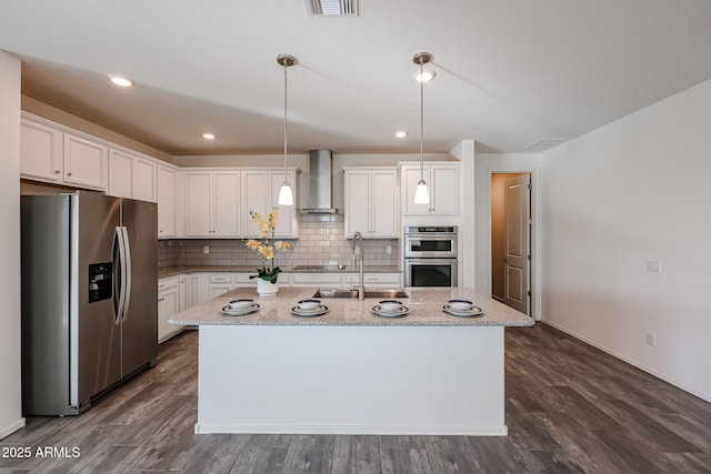 kitchen featuring a kitchen island with sink, white cabinets, wall chimney exhaust hood, and appliances with stainless steel finishes