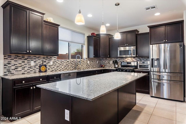 kitchen featuring hanging light fixtures, light stone counters, stainless steel appliances, a kitchen island, and decorative backsplash