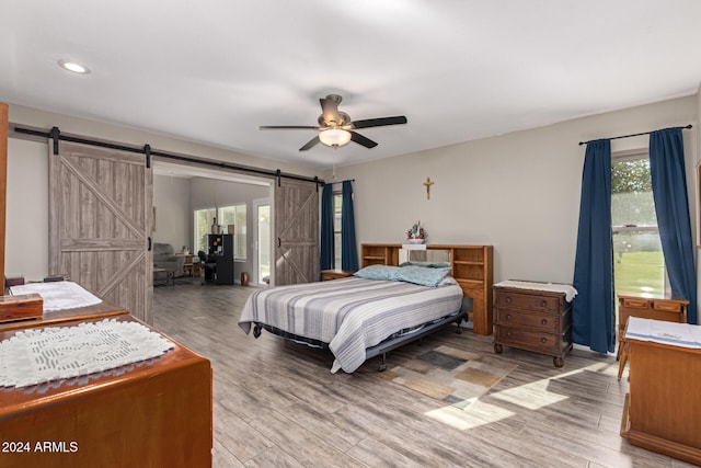 bedroom with wood-type flooring, a barn door, and ceiling fan