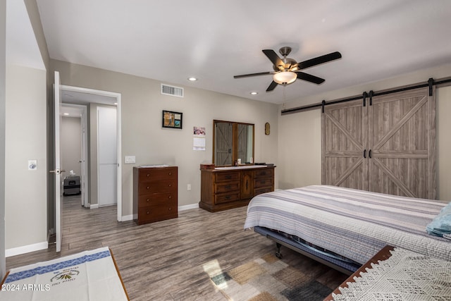 bedroom featuring ceiling fan, a barn door, and wood-type flooring