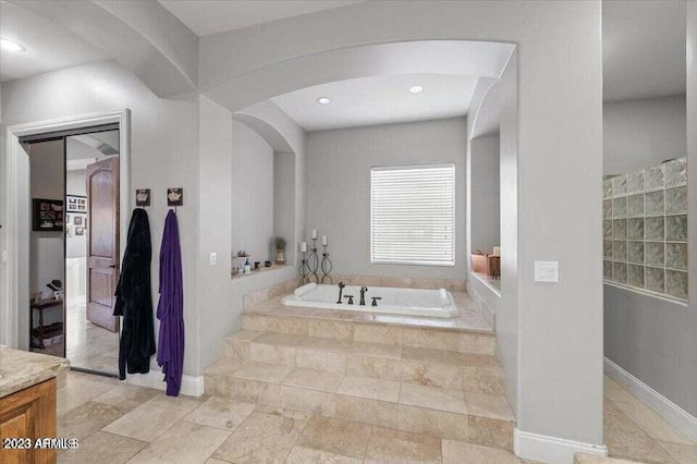 bathroom with tile flooring, tiled tub, and vanity