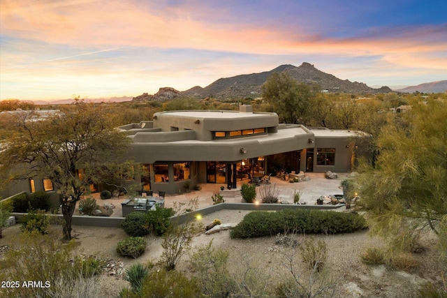 back house at dusk with a mountain view and a patio