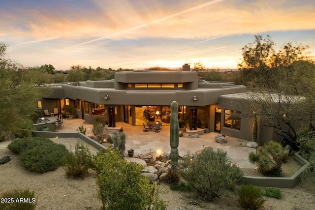 back house at dusk featuring a patio