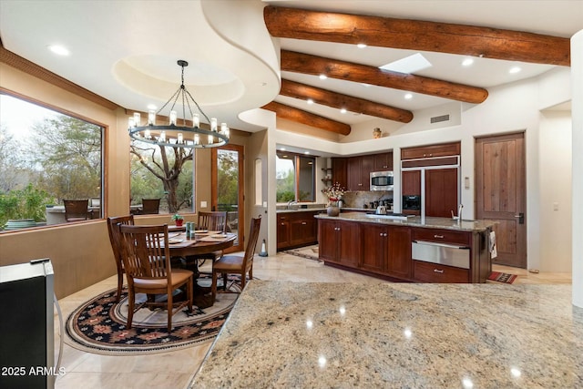 kitchen featuring a chandelier, hanging light fixtures, a center island, built in appliances, and light stone counters