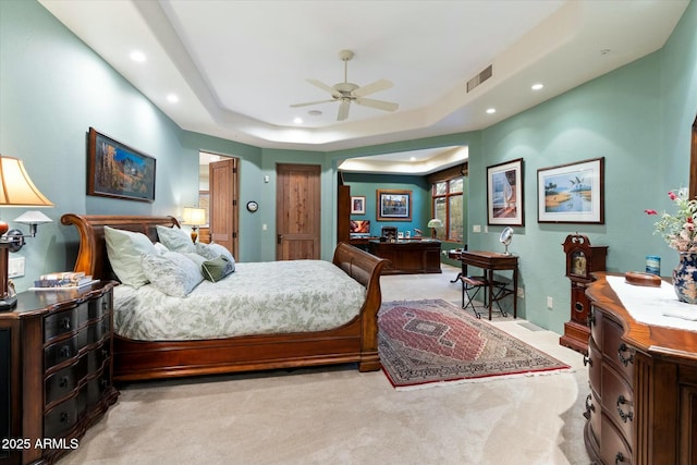 bedroom featuring a raised ceiling, light carpet, and ceiling fan