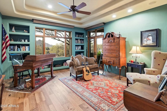 sitting room with a tray ceiling, built in features, french doors, and light wood-type flooring