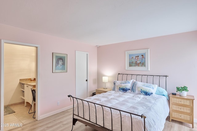 bedroom with baseboards, ensuite bathroom, and light wood finished floors