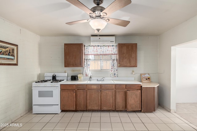 kitchen featuring sink, light tile patterned floors, white range with gas stovetop, ceiling fan, and a wall unit AC