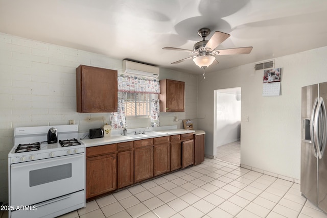 kitchen featuring sink, stainless steel fridge with ice dispenser, light tile patterned floors, an AC wall unit, and white range with gas cooktop