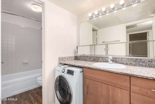 full bath with washer / clothes dryer, toilet, washtub / shower combination, vanity, and wood finished floors