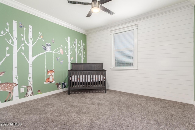 carpeted bedroom with ornamental molding, ceiling fan, a nursery area, and wooden walls