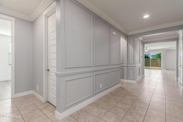 hallway featuring baseboards, ornamental molding, a decorative wall, and light tile patterned floors