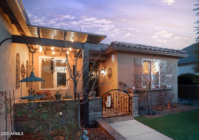 exterior entry at dusk featuring stucco siding, a tile roof, and a gate