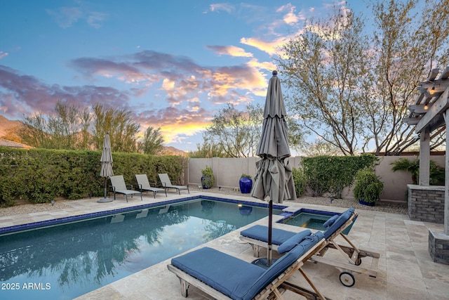 pool at dusk with a patio area and an in ground hot tub