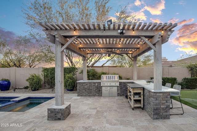 patio terrace at dusk featuring an outdoor kitchen, a pergola, exterior bar, and area for grilling