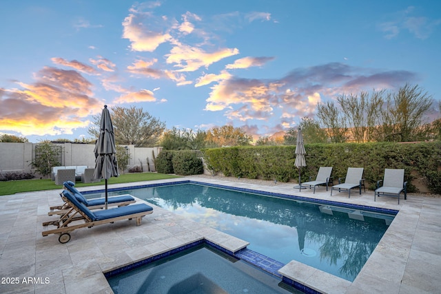 pool at dusk featuring a patio and an in ground hot tub