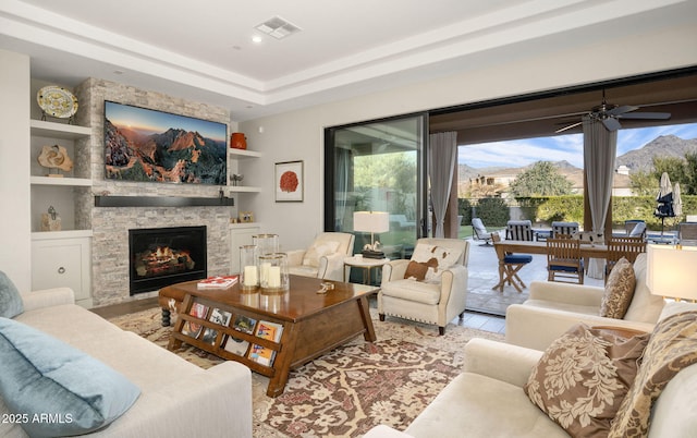 living room featuring ceiling fan, a wealth of natural light, built in features, and a stone fireplace