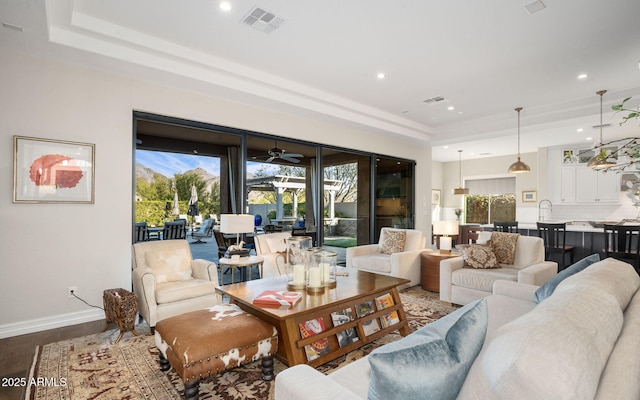 living room with ceiling fan, a tray ceiling, and hardwood / wood-style flooring