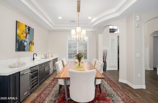 dining area with beverage cooler, a raised ceiling, dark wood-type flooring, sink, and an inviting chandelier