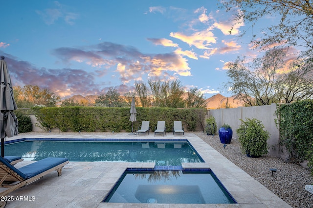 pool at dusk featuring a patio, an in ground hot tub, and a mountain view