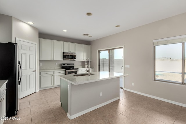 kitchen featuring a center island with sink, sink, white cabinetry, stainless steel appliances, and light stone counters