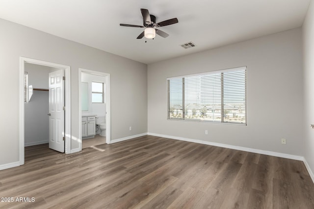 unfurnished bedroom featuring ensuite bathroom, ceiling fan, dark hardwood / wood-style floors, a walk in closet, and a closet