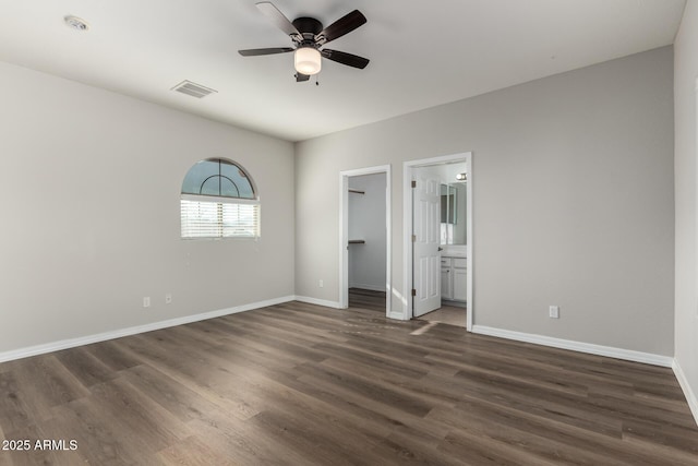 unfurnished bedroom with ensuite bathroom, ceiling fan, a spacious closet, dark wood-type flooring, and a closet