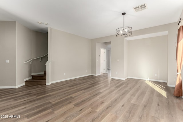 empty room with wood-type flooring and a notable chandelier