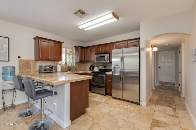 kitchen with a breakfast bar area, stainless steel appliances, a peninsula, light countertops, and decorative backsplash