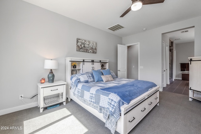 bedroom with a barn door, dark colored carpet, and ceiling fan