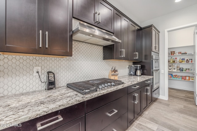 kitchen featuring appliances with stainless steel finishes, tasteful backsplash, light stone countertops, light hardwood / wood-style flooring, and dark brown cabinetry