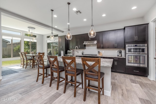 kitchen featuring dark brown cabinetry, a kitchen island with sink, hanging light fixtures, and light hardwood / wood-style floors