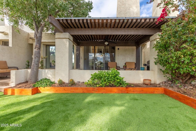 back of property with a yard, stucco siding, and a ceiling fan