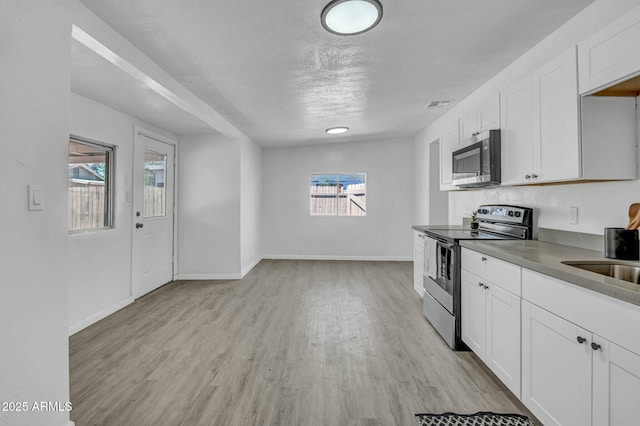 kitchen featuring stainless steel appliances, plenty of natural light, light wood finished floors, and baseboards