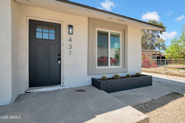 doorway to property with stucco siding, fence, and a patio