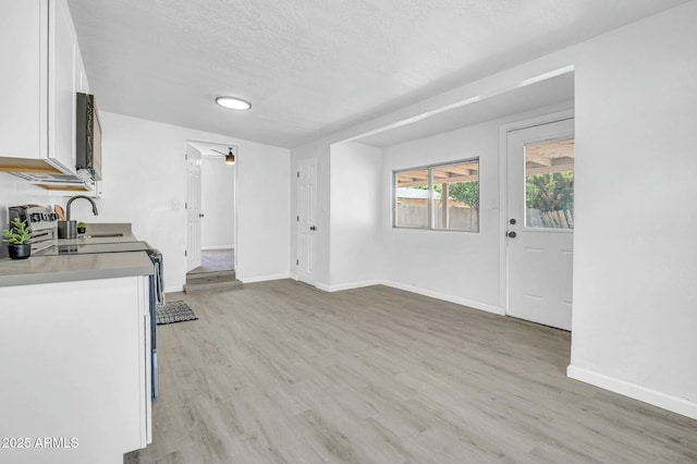 kitchen featuring baseboards, white cabinets, light wood-style flooring, and a sink