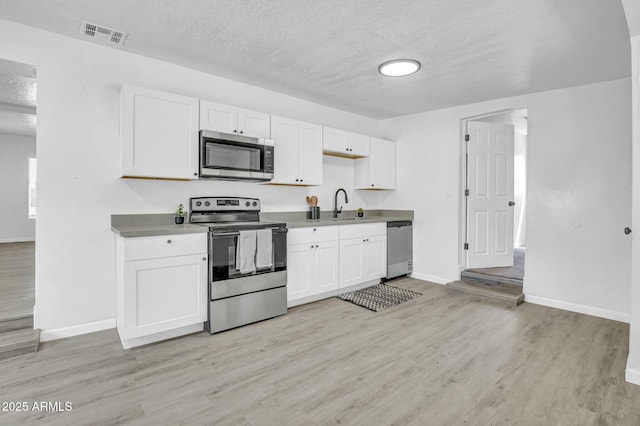 kitchen featuring a sink, appliances with stainless steel finishes, visible vents, baseboards, and light wood-type flooring