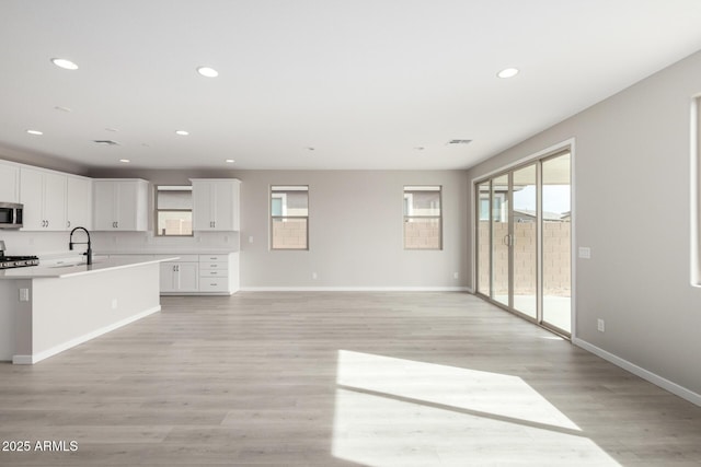 kitchen with tasteful backsplash, sink, white cabinets, stove, and light wood-type flooring