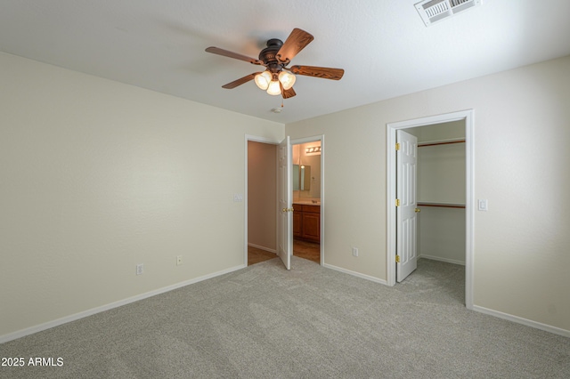 unfurnished bedroom with baseboards, visible vents, ensuite bath, light carpet, and a walk in closet