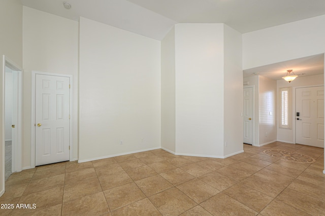 spare room featuring light tile patterned floors, baseboards, and high vaulted ceiling