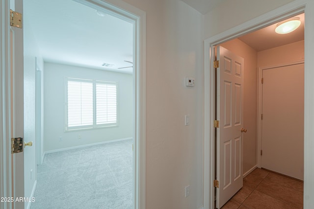 hallway with tile patterned floors, visible vents, baseboards, and carpet